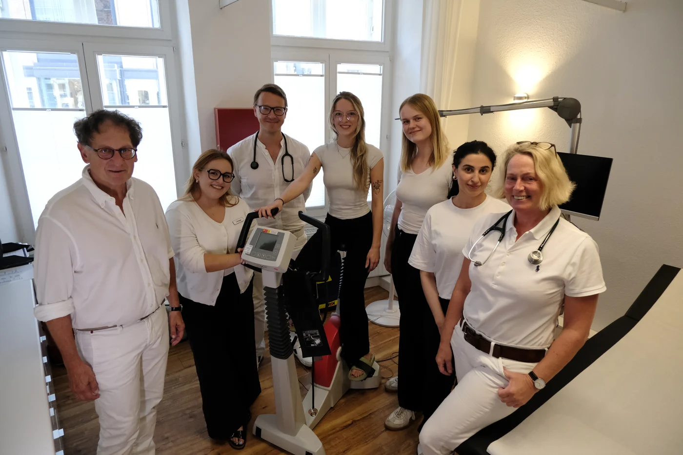 Das Team im Behandlungsraum am Ergometer, alle in Weiß