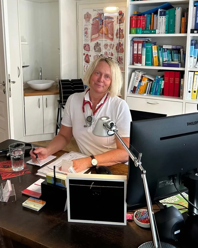 Dr. med. Maike Klingler am Schreibtisch in ihrem Sprechzimmer, dahinter die Bücherwand