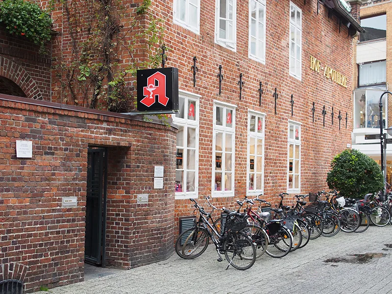 Das Backsteinhaus in der Fußgängerzone, Fahrräder davor, Apothekenzeichen an der Fassade